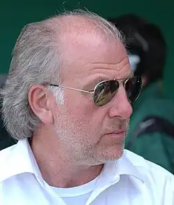 Photo de droit de David Richards, un homme à lunettes de soleil, chemise blanche, cheveux blancs et légèrement barbu