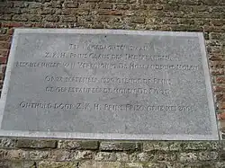 Photographie en couleurs d'une plaque rectangulaire en pierre gris clair incorporée à un mur en brique et portant des inscriptions.