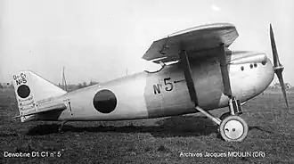 Photographie en noir et blanc d'un avion à hélice vu de côté, posé sur l'herbe.