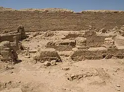 Photo en couleur. Dans le désert, des vestiges en pierres taillées sont à l'avant-plan.