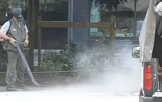 Une souffleuse portative, en nettoyant le sol, disperse dans l'atmosphère de la poussière.