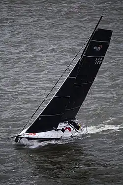 Vue aérienne d'un bateau bleu et blanc filant avec un ris dans la grand-voile.