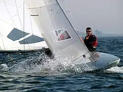 Vu de trois quarts avant, progressant à la voile, bateau à l'avant très large, très arrondi et très plat.