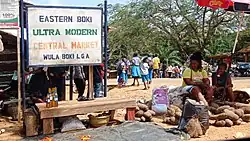 scène de marché, avec des articles disposés au sol et un panneau indiquant la zone géographique