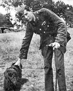 Photo noir et blanc montrant Edward Mannock debout se penchant pour carresser un chien. Il s'appuye sur une canne.