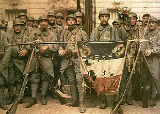 Autochrome du 114e régiment d'infanterie à Paris, le 14 juillet 1917, le drapeau français déployé et posé sur des armoiries.