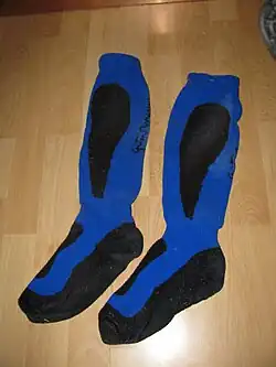 Des chaussettes bleu vif avec des bandes noires au niveau des mollets et de la plante des pieds sont posées sur un plancher.