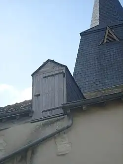 Photographie en couleurs d'une lucarne percée d'une porte en bois dans un toit.