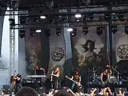 Groupe entouré de drapeaux joue un concert devant un public.