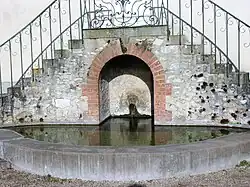Photographie d'une source s'écoulant dans un bassin sous un double escalier.