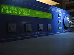 Vue latérale d'une machine rectangulaire bleue, avec quelques potentiomètres et un écran LCD affichant "real chorus" et "detune"