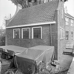 Photographie en noir et blanc d'une remise couronnée d'un pignon et précédée d'un terrain vague.