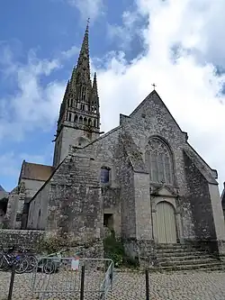 Photographie d'une façade d'église à deux niveaux, avec un portail de style classique surmonté d'une grande fenêtre de style gothique rayonnant