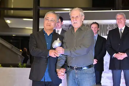 deux hommes se serrent la main en se donnant une statuette