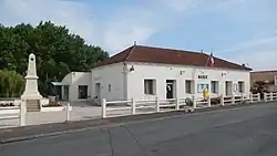 La mairie de Cabariot (un bâtiment blanc sans étage, assez simple), avec, à sa gauche, le monument aux morts de la commune.