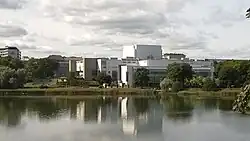 Bâtiment blanc, moderne, avec de grandes baies vitrées, se reflètant dans l’eau d’un lac.