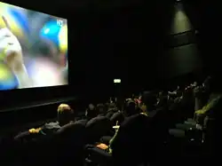 Photo d'une salle de cinéma encore éclairée en pleine projection d'un match de football en haute définition.