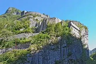 Vue d’un fort à flanc de falaise, envahi par la végétation.