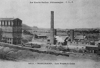 Un haut bâtiment industrielle sur la gauche, d'autres plus petit à droite surmontés d'une haute cheminée.
