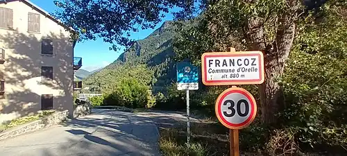 Photographie d'un panneau de Francoz, écrit en noir, où la limitation de vitesse est de 30&nbsp;km/, devant des immeubles.