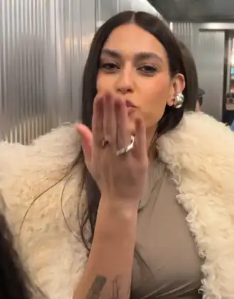 chantuse Gaia, vêtue d'un manteau de fourrure donnant un baiser à la caméra dans un ascenseur