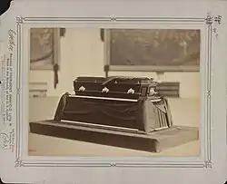 Photographie en noir et blanc d'un cercueil reposant sur un catafalque