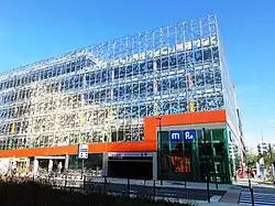 Immeuble à façade en verre et panneaux oranges abritant le parc relais de la station de métro Les Gayeulles, elle-même située sous le bâtiment. La photo est prise du côté où se situe l'accès des voitures.