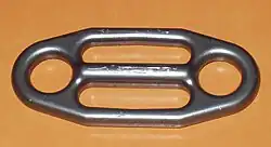 Une plaquette Gi-Gi, présentant un orifice rond de chaque côté, et deux orifices allongés au centre.