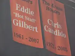Deux bannières orange suspendu au plafond d'une salle. Sur celle de gauche est écrit Eddie Gilbert et sur la seconde Chris Candido.