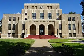 Vue d'un bâtiment de pierres grises, avec une entrée faite de trois arches.