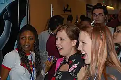 Photographie couleurs de 3 jeunes filles au premier plan d'une foule. L'une est noire, les deux autres blanches. Elle sont concentrées