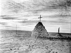 Photographie noir et blanc d'un monticule de neige, surmonté d'une croix.