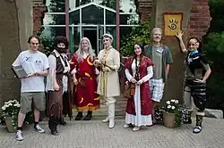 Photo de sept personnes devant une entrée, dont 5 en cosplay des personnages du jeu.