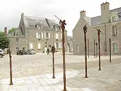 Vue d'une place, aux façades de granit, avec des statuettes surmontant des colonnes.