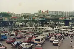 La place à l'est de la gare de Canton en 1991. On peut remarquer la prédominance des caractères chinois traditionnels dans les logos des marques de cette époque, notamment Jianlibao&nbsp;(en) (健力寶), Rejoice (飄柔) et 萬家樂 ; seule Head & Shoulders (海飞丝) est imprimé en caractères simplifiées. En Chine continentale, il était autorisé de concevoir des logos de marque en caractères traditionnels, mais depuis 2020, à l'exception de Jianlibao&nbsp;(en), les trois autres sont passés au simplifié.