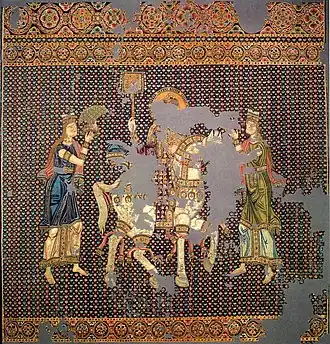 Photographie d'une tapisserie en soie dégradée représentant trois personnages, dont un à cheval.