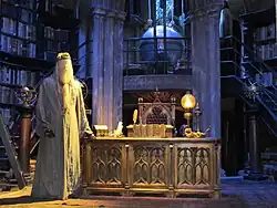 Un bureau sur deux niveaux, dans une salle semblant circulaire, avec des livres recouvrants les murs à droite et à gauche. Au centre et au niveau supérieur, derrière une balustrade, est visible un grand globe. Un mannequin vêtu d'une robe de sorcier grise se tient près du bureau en bois présent au centre du niveau inférieur