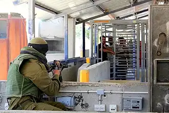 Soldat israélien face à des Palestiniens attendant au check-point d'Hawara en Cisjordanie occupée.