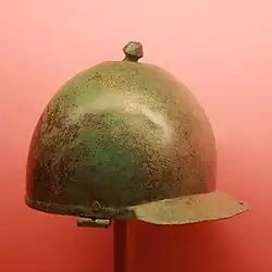 Photographie d’un casque en bronze légèrement terni et cabossé.