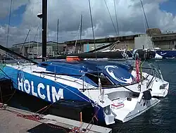Voilier vert, bleu et blanc vu de trois quarts arrière, amarré au ponton.