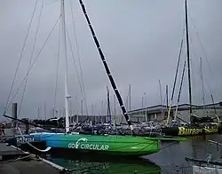 Vu de trois quarts avant, voilier à foils vert et bleu amarré au ponton.