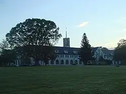 Photographie couleur d'un bâtiment entouré d'arbres et de pelouses au crépuscule.