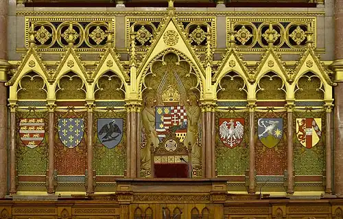 Derrière le pupitre du président de la Chambre des magnats sont représentés les blasons des principales familles ayant régné sur la Hongrie. Encadrant les armes du royaume, de gauche à droite : Arpadiens, Anjou, Hunyadi, Jagellons, Zapolya, Habsbourg.