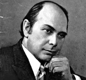 Photo en noir et blanc d'un homme en buste, de trois quarts, le menton sur le poing.