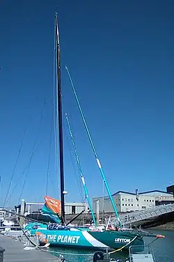 Vu de trois quarts avant, en entier, voilier à foils bleu, blanc et vert amarré au ponton.