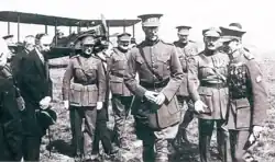 Photographie noir et blanc de divers hommes en uniformes marchant. Un avion se trouve à l'arrière plan.