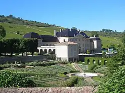La photo couleur représente un château devant lequel s'étend un jardin à la française. En arrière-plan, le coteau est couvert de vignes.