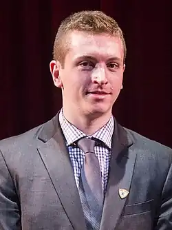 Un jeune homme en costume-cravate avec un léger sourire.