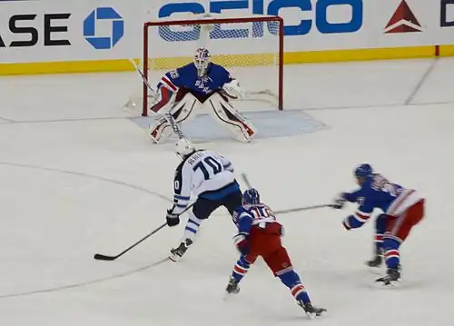 Photographie d'une partie de patinoire avec trois joueurs avec un uniforme de hockey bleu et un avec un uniforme blanc en train de tirer au but.