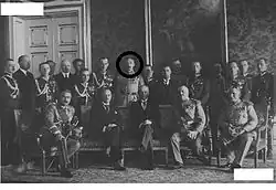 Photographie officielle avec personnalités militaires et politiques posant dans un salon, les uns, debout, les autres assis dans un canapé.